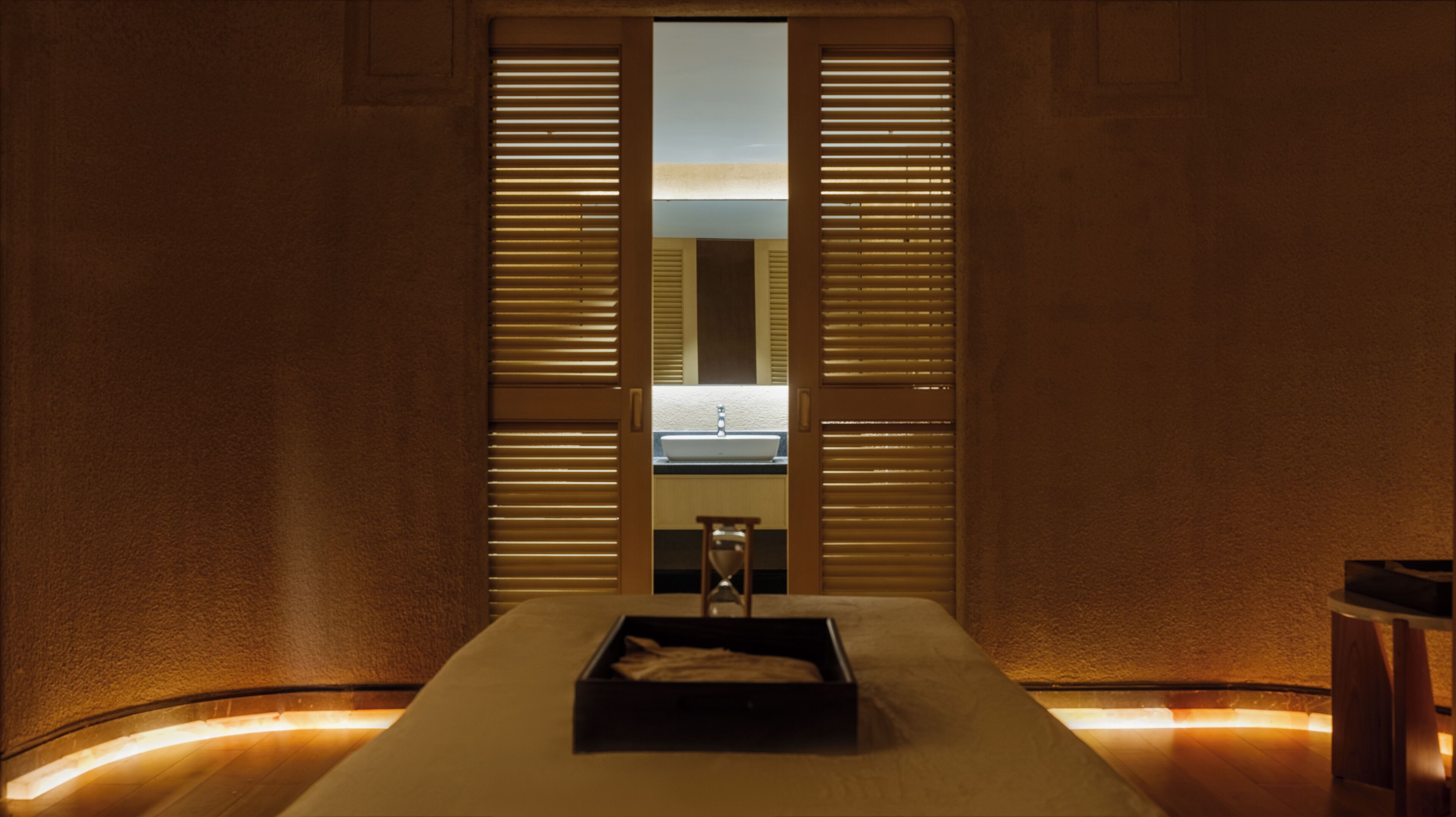 A dimly lit room with a large window, a sink, and a small stool.