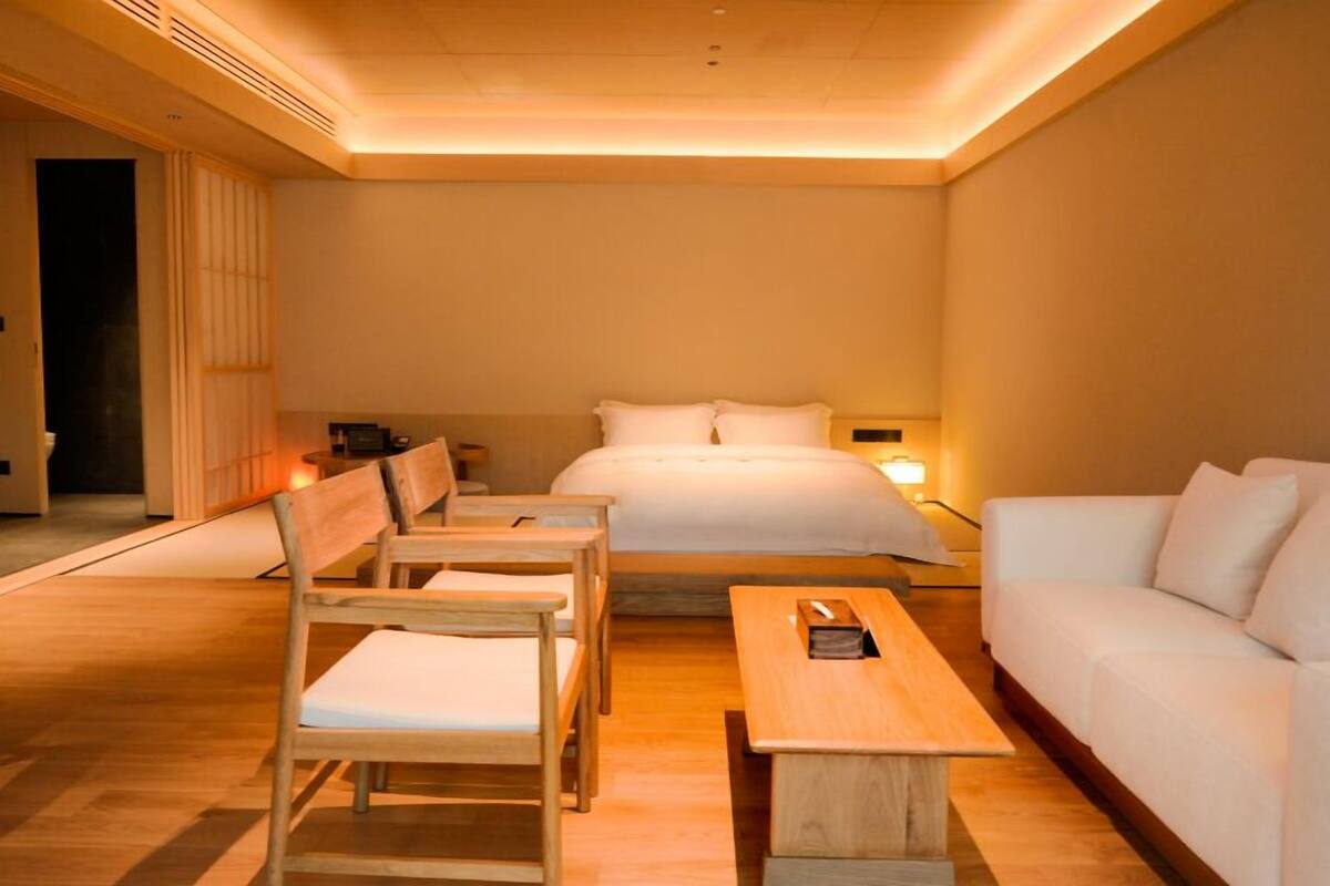 Una habitación de hotel con una cama, dos sillas de madera, una mesa de madera y un sofá blanco.
