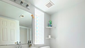 Een badkamer met een witte wastafel, een spiegel, een toilet en een raam.