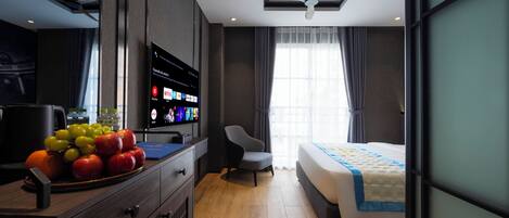 A modern hotel room with a bed, a desk with a fruit bowl, a television, and a ceiling fan.