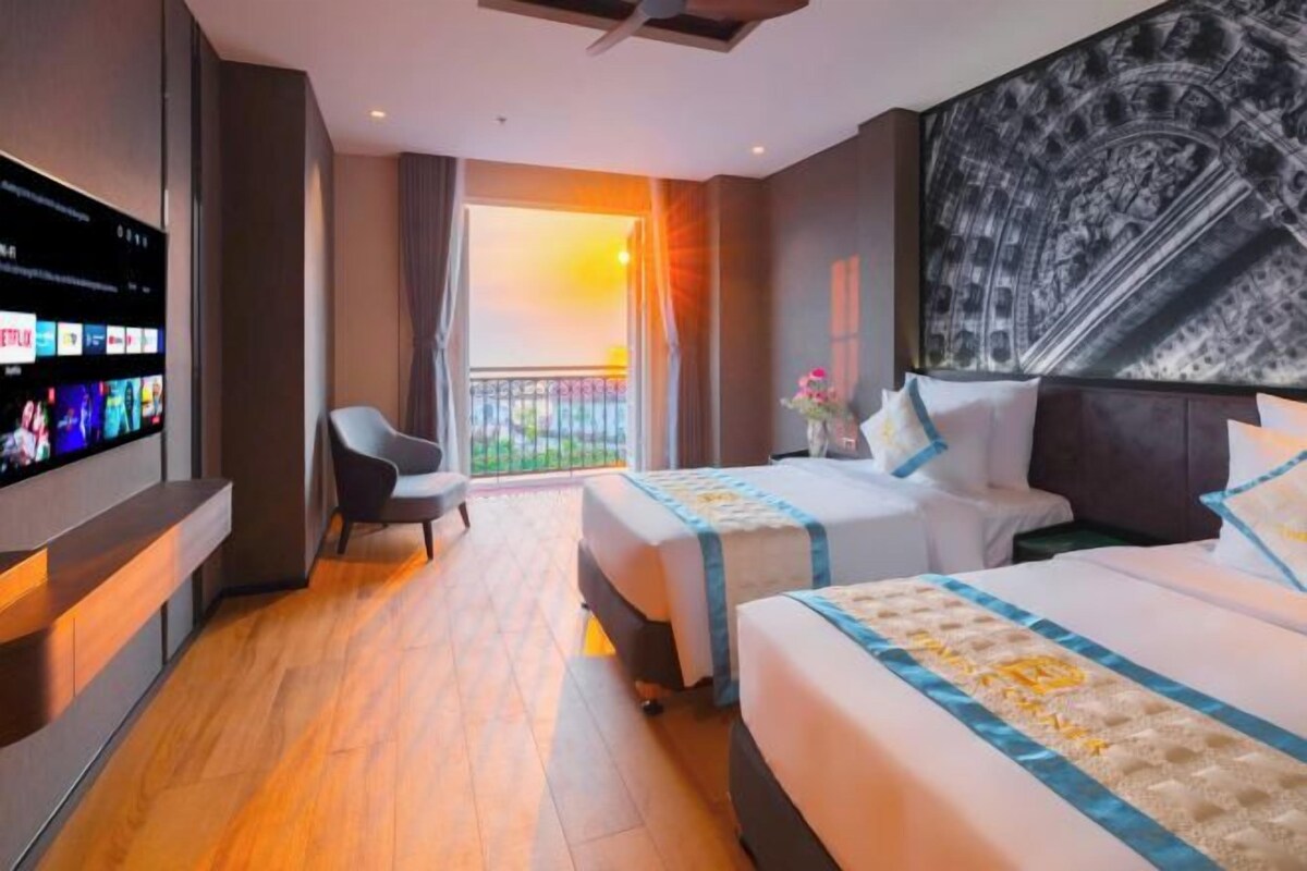A hotel room with two beds, a TV, a balcony, and a large artwork on the wall.