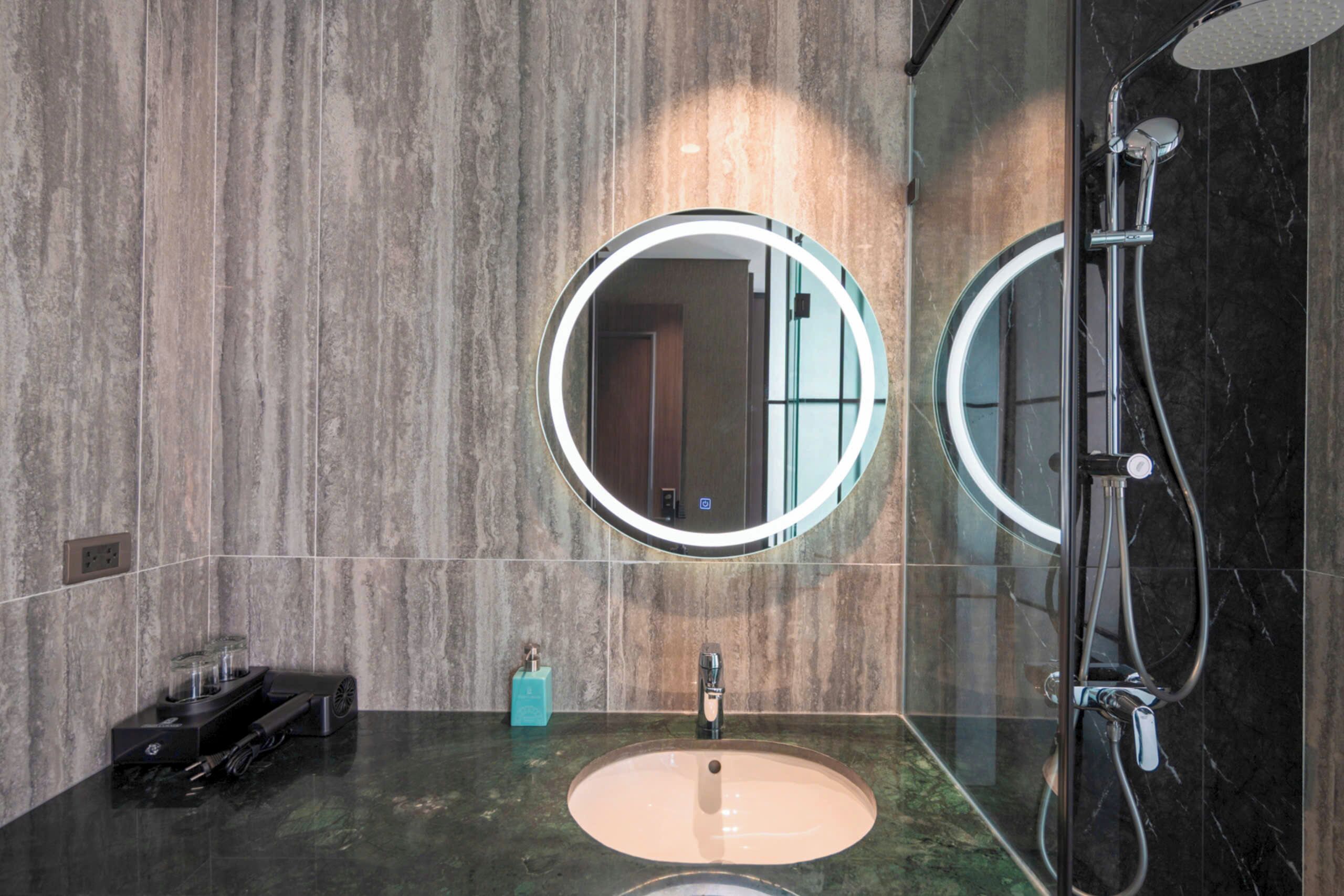 A modern bathroom with a round mirror, a sink, and a shower.