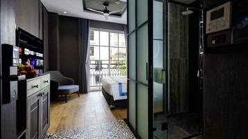 A modern hotel room with a large TV displaying streaming services, a comfortable chair, a bed with a view through a glass door, and a shower area.