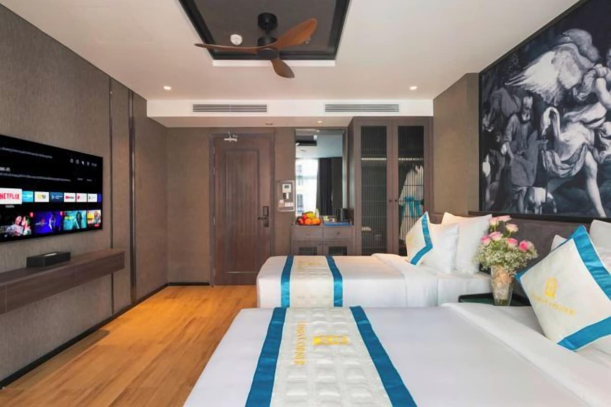 A modern hotel room with a large bed, a flat-screen TV mounted on the wall, and a ceiling fan.