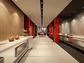 Un pasillo moderno de hotel con un largo mostrador de recepción, detalles en rojo y una zona de estar central.