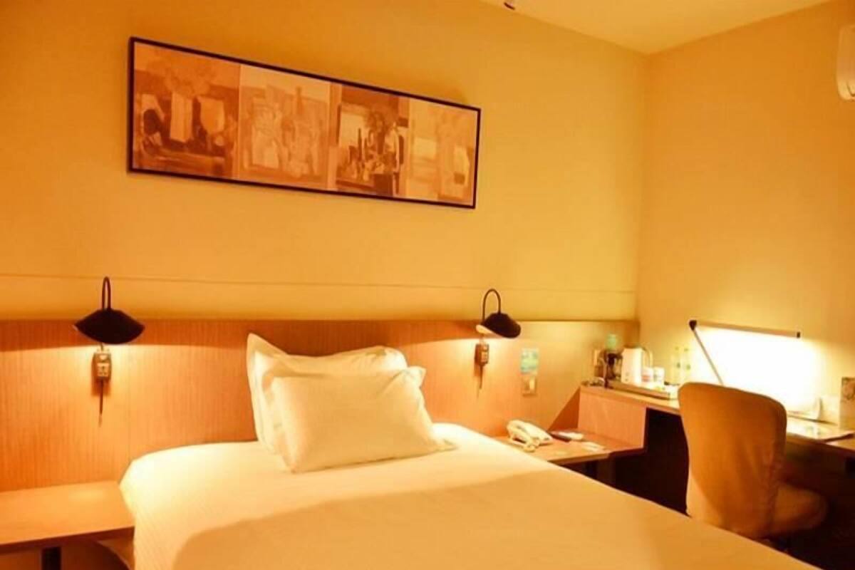 A hotel room with a bed, bedside tables, a desk with a lamp, and a wall-mounted picture.
