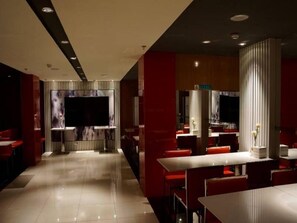 En moderne restaurant med en lang bardisk, røde siddepladser og et stort tv-skærm.