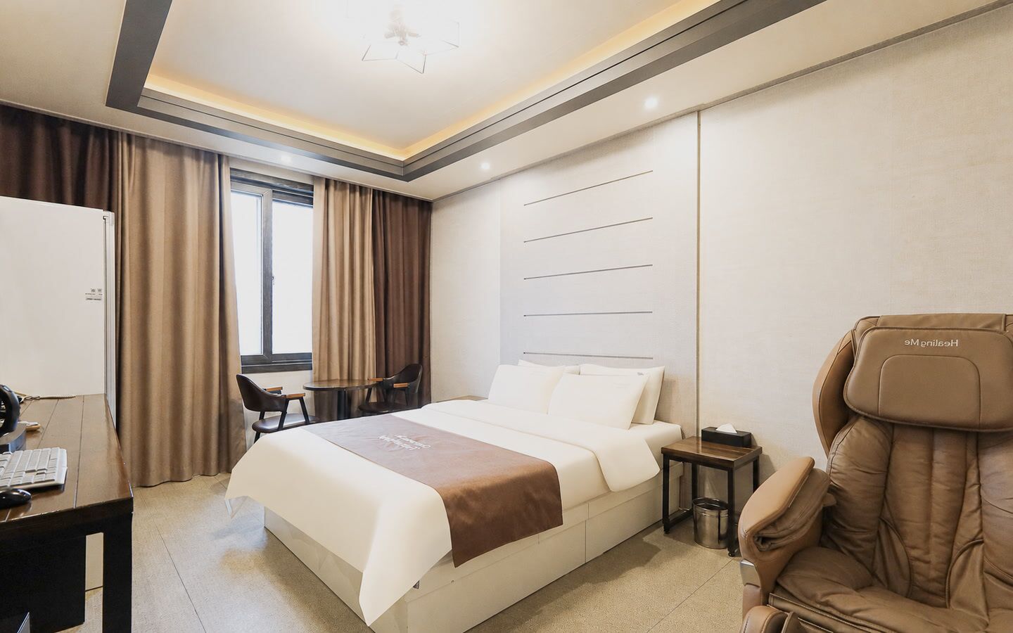 A hotel room with a bed, desk, chair, and massage chair.