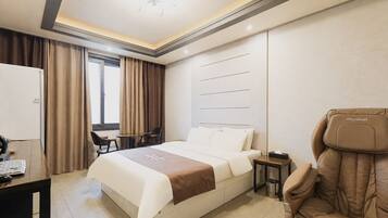 A hotel room with a bed, desk, chair, and massage chair.