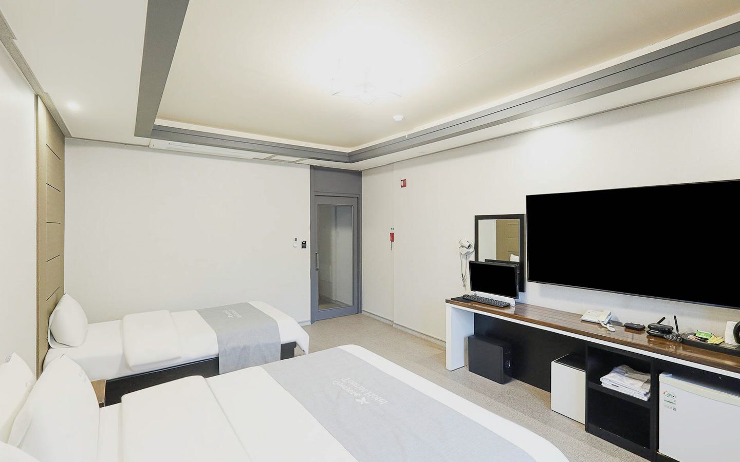 A hotel room with a bed, a desk with a computer, a television, and a door.