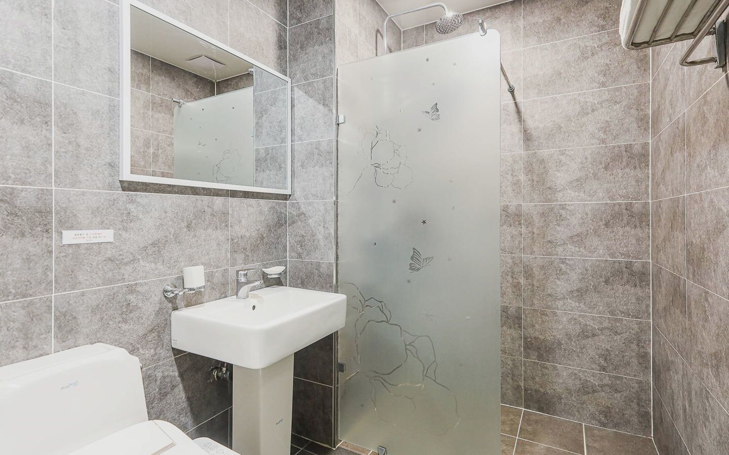 Un baño con lavamanos blanco, un espejo y una ducha con puerta de vidrio esmerilado.