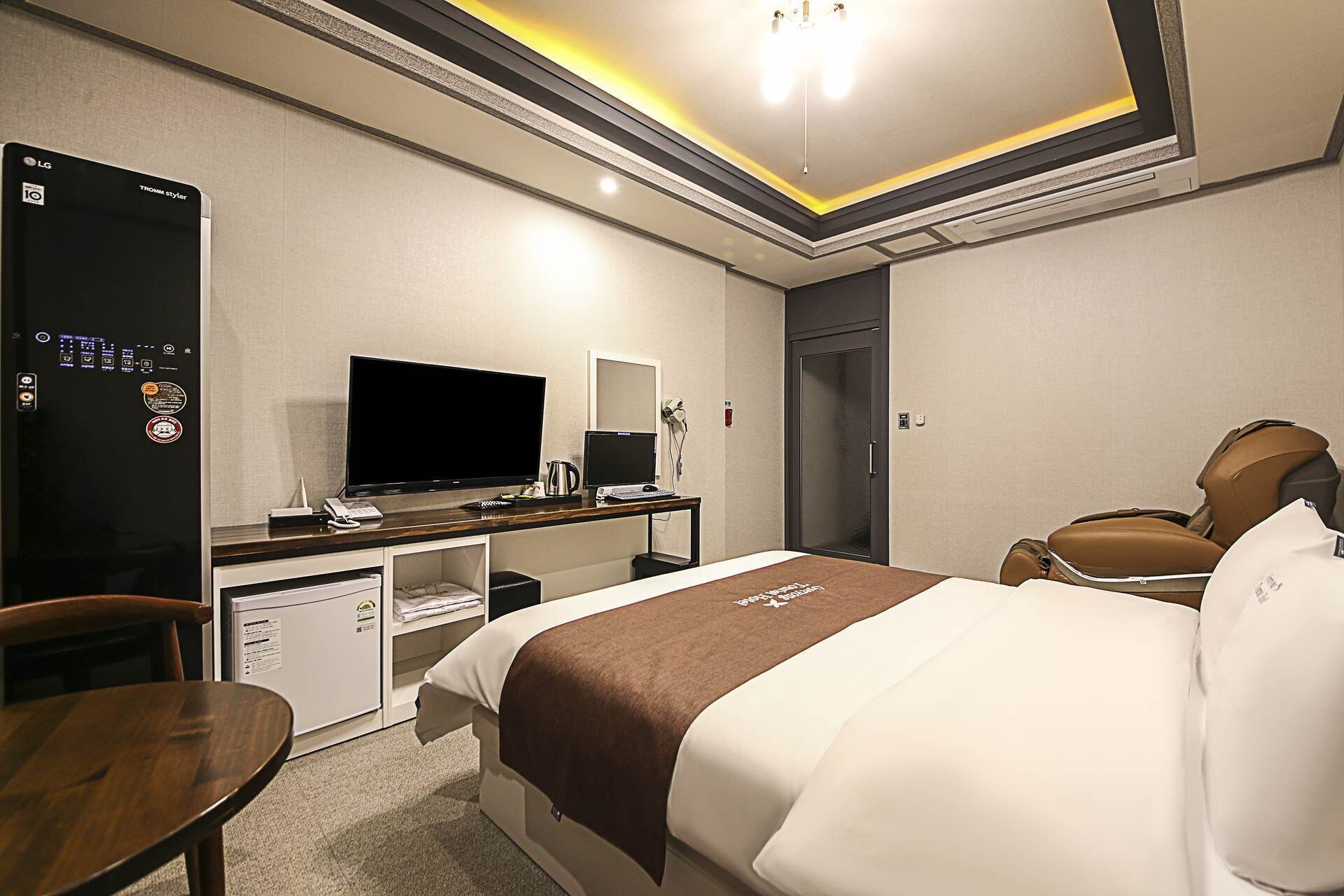 A hotel room with a bed, a desk with a TV, a computer, a mini-fridge, and a chair.
