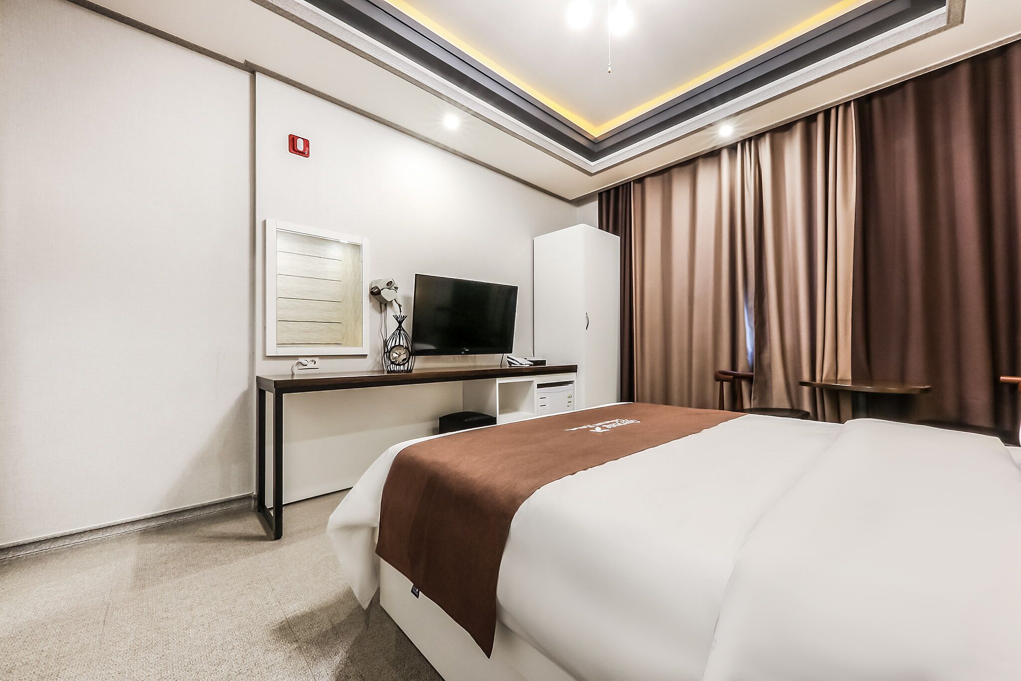 Una habitación de hotel con cama, escritorio con televisor, armario y señal roja de salida de emergencia.