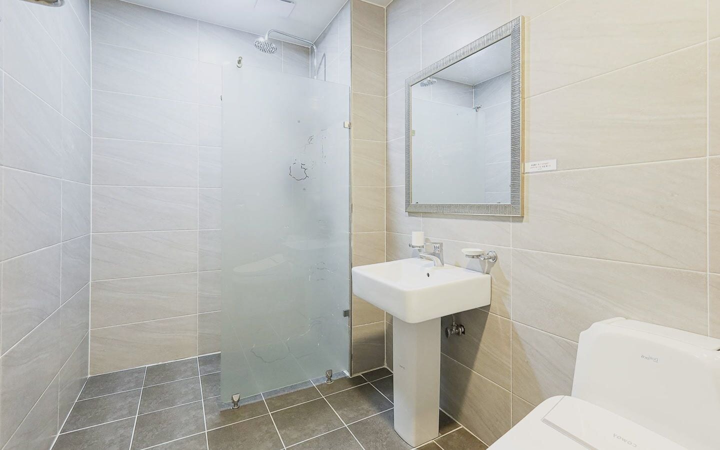 Een badkamer met een douchecabine van glas, een wastafel op een voetstuk en een spiegel boven de wastafel.