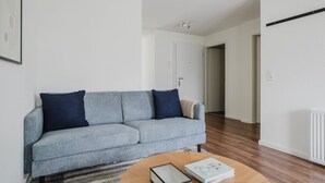 A living room with a grey sofa, two dark blue cushions, a wooden coffee table with books and a box, and a white door in the background.
