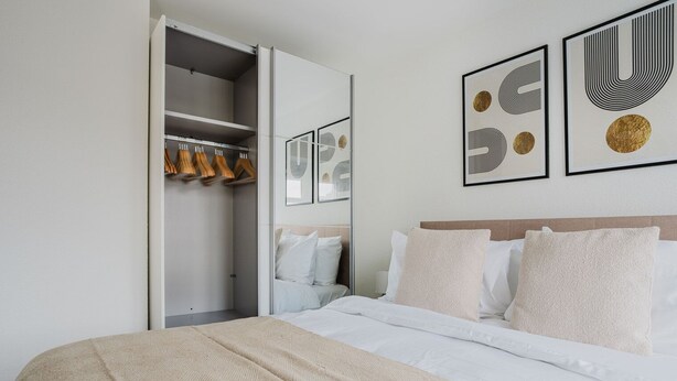 A hotel room with a bed, a wardrobe, and artwork on the wall.