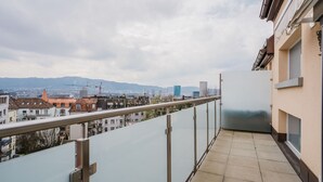 A balcony with a city view, including buildings and mountains in the distance.