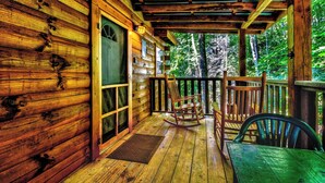 A wooden cabin with a porch, rocking chairs, and a table.