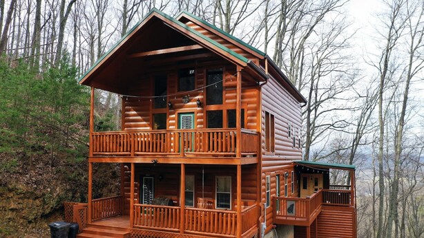 Une cabane en rondins à deux étages, dotée d’un balcon et entourée d’arbres.