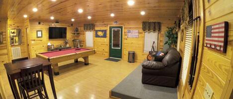 A cozy cabin interior with a pool table, a sofa, and a television.