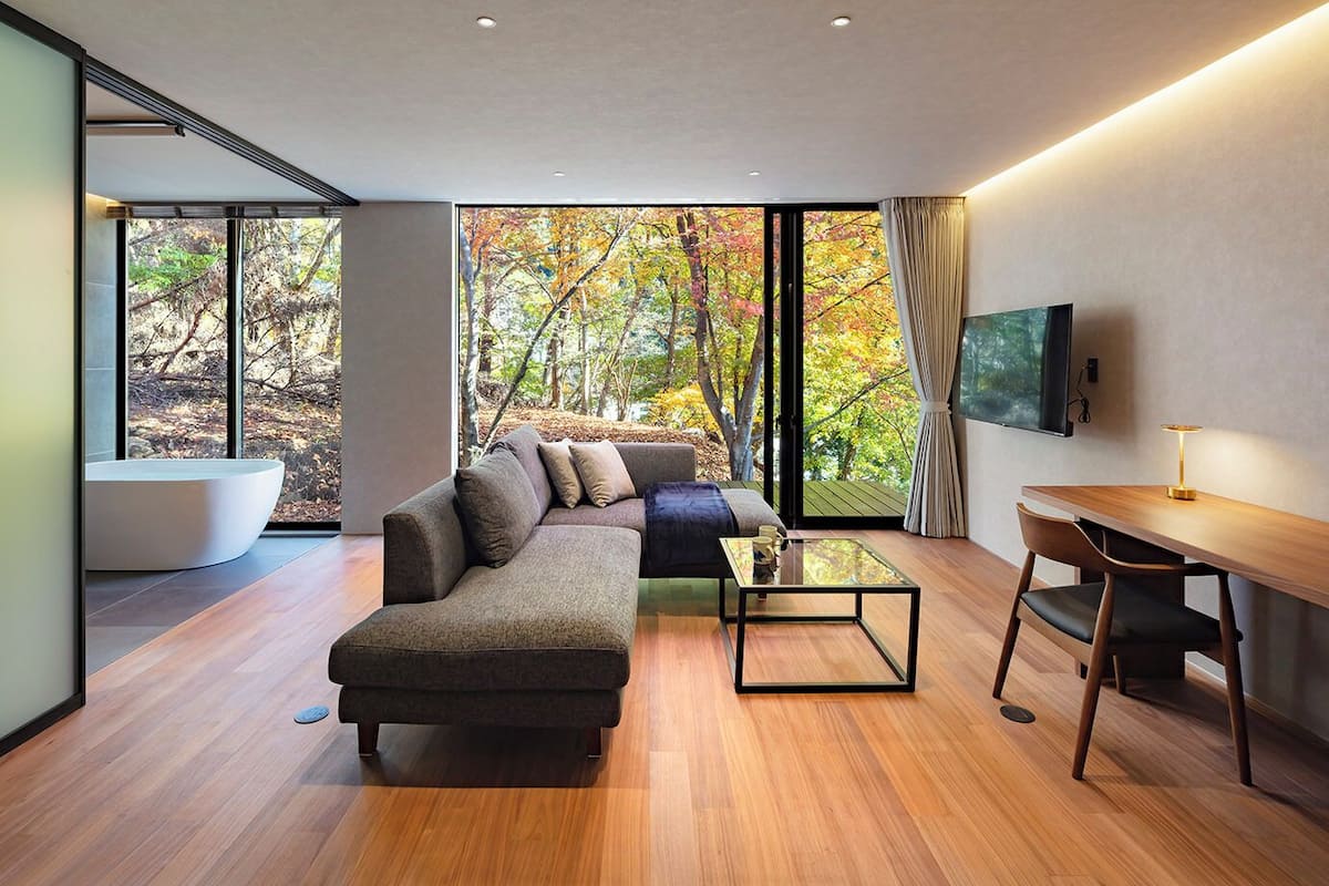 A modern living room with a sectional sofa, a glass coffee table, and a wooden desk.