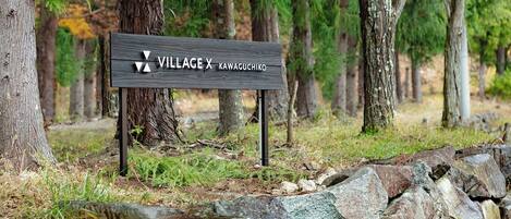 A wooden sign with the text "VILLAGE X KAWACHIKO" in a forest setting.
