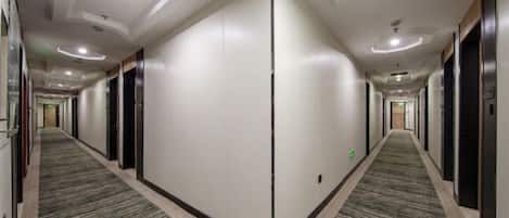Un pasillo de hotel con suelo alfombrado, puertas a ambos lados y techo con iluminación empotrada.