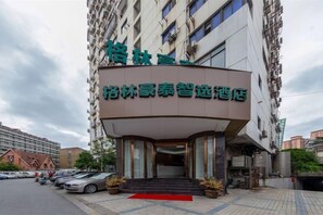 A hotel entrance with a curved facade, a red carpet, and a parking lot with cars. - GreenTree Smart Choice Hotel (Shanghai Chest hospital Hongqiao Road Metro Station) (Shanghai)