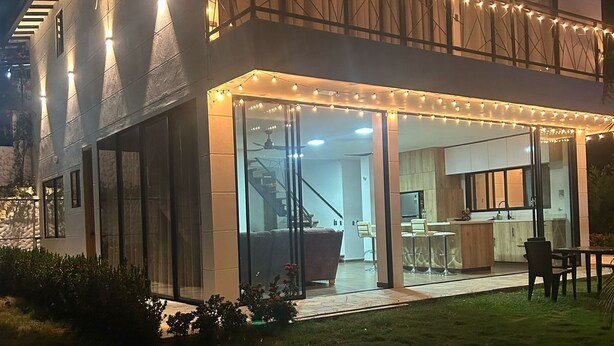 A modern two-story house with a glass entrance, outdoor seating, and string lights.