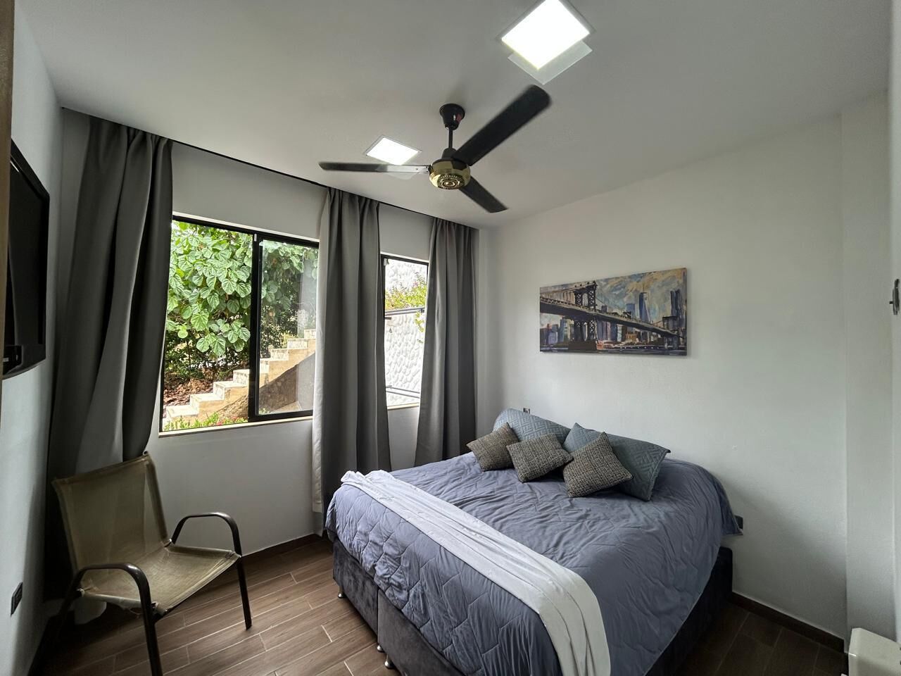 A bedroom with a bed, a chair, a ceiling fan, and a window with curtains.
