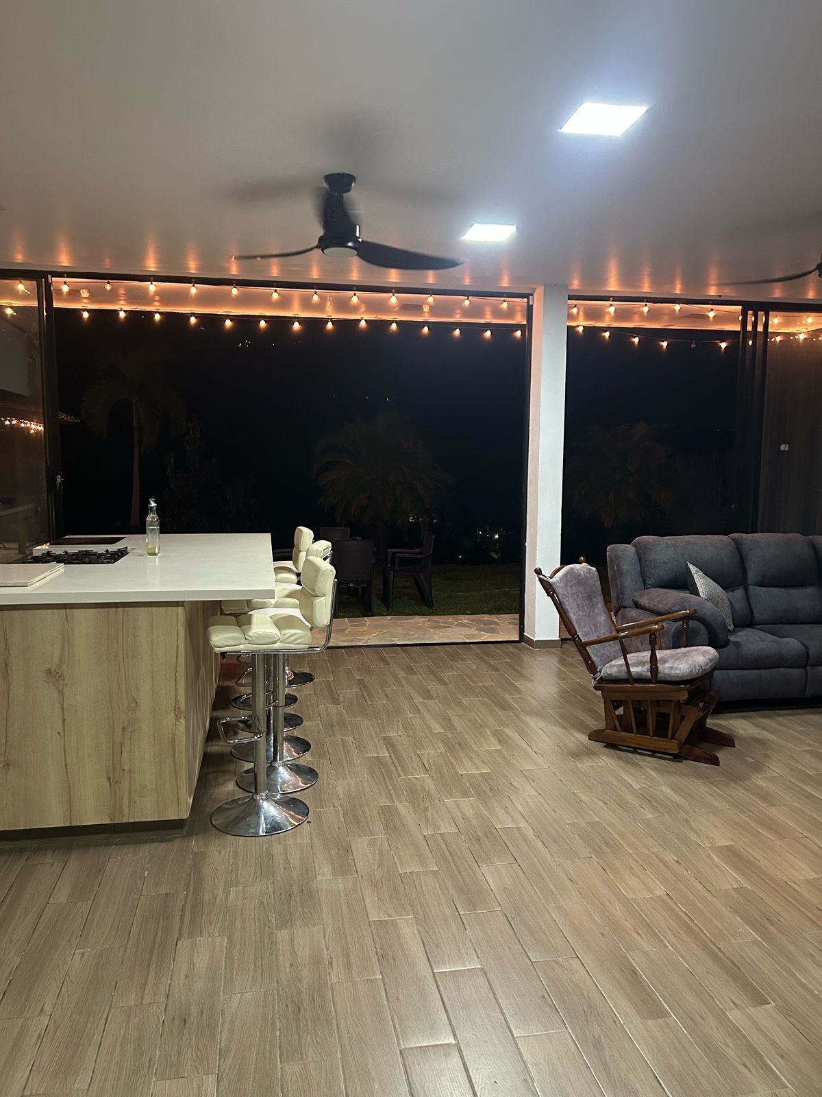 Un espacio exterior con bar, asientos e iluminación de luces colgantes.