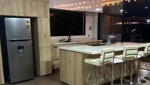 A modern kitchen with a central island, bar stools, a refrigerator, and a large window.