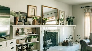 A living room with a fireplace, shelves with decorative items, and a television. - Charming 2-bedroom house in quiet country Visalia with pool (Visalia)