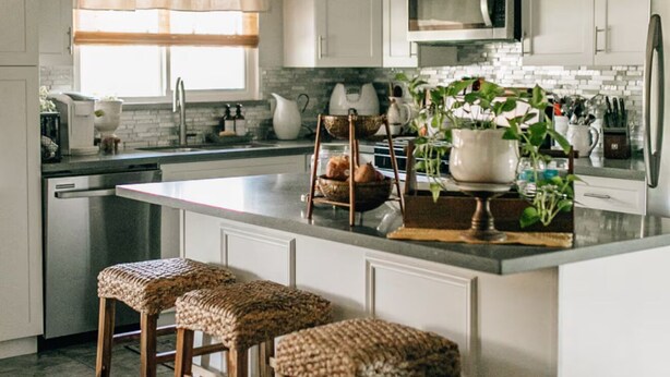 A modern kitchen with white cabinets, a stainless steel refrigerator, a microwave, and a large island with bar stools. - Charming 2-bedroom house in quiet country Visalia with pool (Visalia)