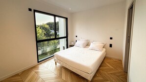 Un dormitori modern amb una finestra gran, un llit amb roba de llit blanca i un sòl de fusta amb relleu de petxina.