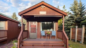 A wooden cabin with a porch, a door, and two chairs.