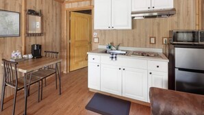 A compact kitchen with wooden walls, white cabinets, a stainless steel refrigerator, and a coffee maker on the counter.