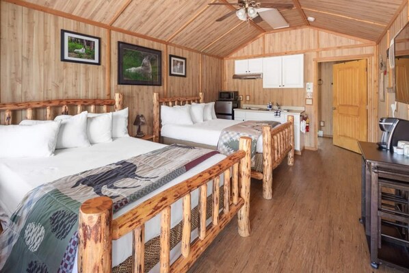 A cabin-style room with two beds, a kitchenette, and wooden walls.