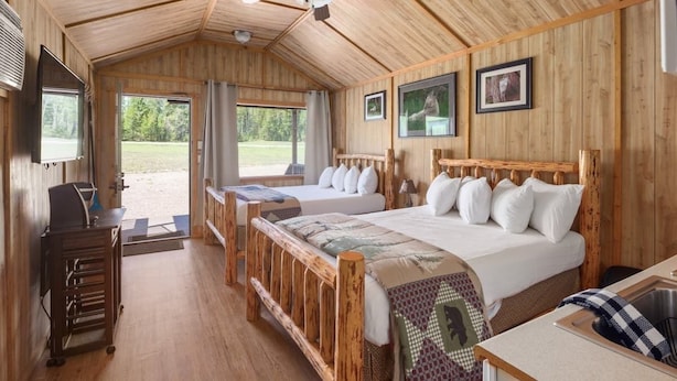 A wooden cabin-style bedroom with two beds, a desk, and a television. - Wolf Cabin! 6 miles to Glacier! (Coram)