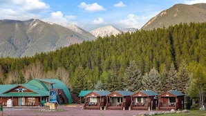A lodge with a green roof, wooden cabins, and a mountain backdrop. - Wolf Cabin! 6 miles to Glacier! (Coram)