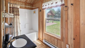 A wooden cabin bathroom with a bathtub, a sink, and a window with a view of a garden. - Wolf Cabin! 6 miles to Glacier! (Coram)