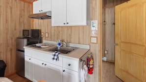 A compact kitchen with white cabinets, a microwave, a sink, and a fire extinguisher. - Wolf Cabin! 6 miles to Glacier! (Coram)