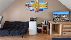 Un espacio habitable compacto con sofá, una kitchenette pequeña, televisor y una obra de arte colgada en la pared.