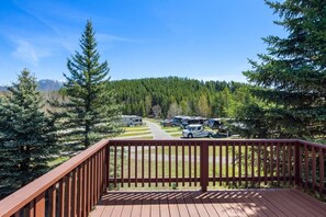 A wooden deck overlooking a campground with RVs parked on a gravel road, surrounded by dense forest and mountains in the background. - Mountain View Studio! 6 Miles to Glacier! (Coram)
