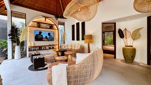 A modern living room with a TV, comfortable seating, and a large window. - Villa Pacha Seminyak (Seminyak)