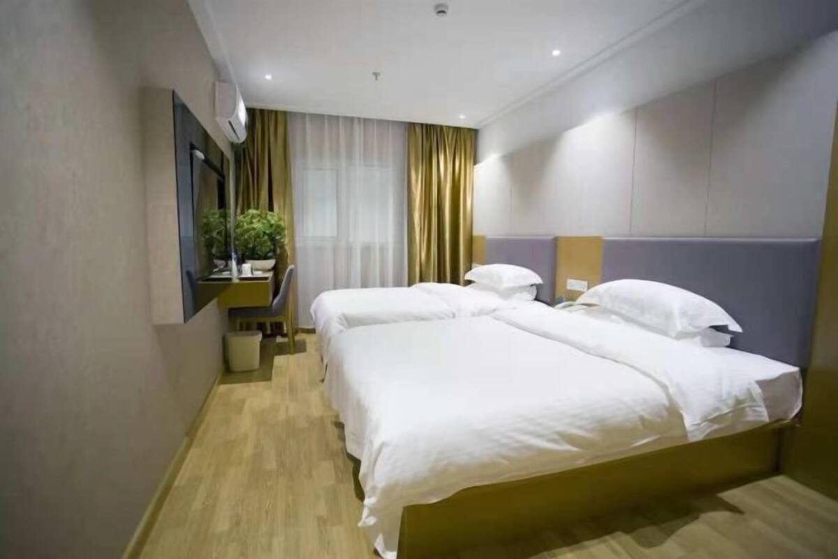 Et hotelværelse med to senge, et skrivebord med stol, en potteplante og et stort spejl.