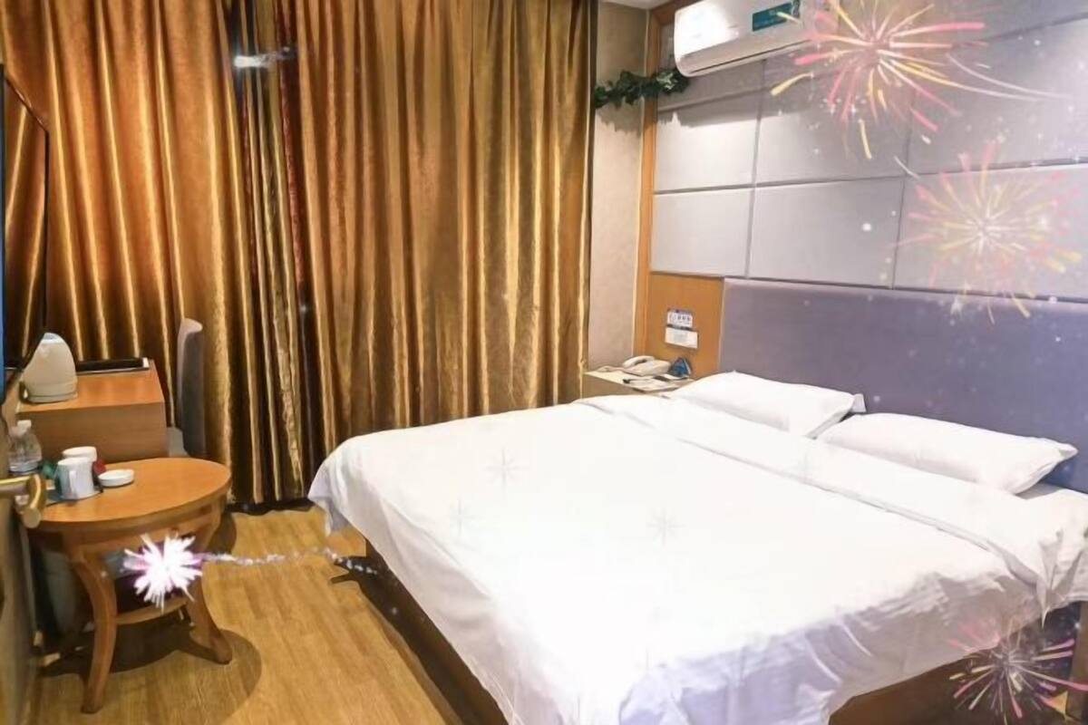Et hotelværelse med seng, et sengebord, en lampe, en telefon og gardiner.