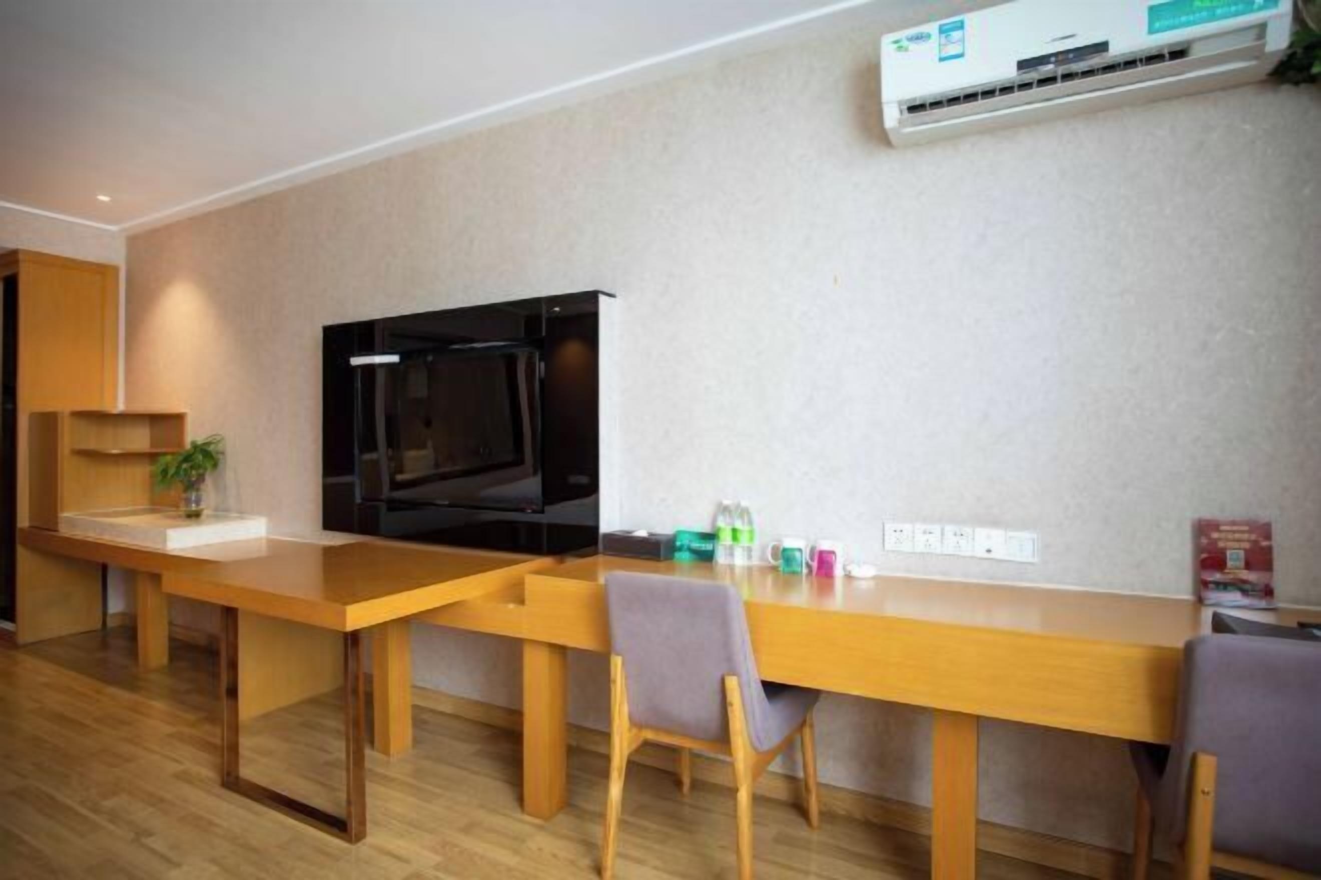 A modern living room with a wooden dining table, two chairs, a flat-screen TV, and an air conditioning unit on the wall.