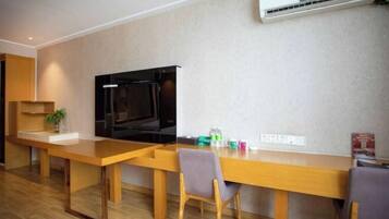 A modern living room with a wooden dining table, two chairs, a flat-screen TV, and an air conditioning unit on the wall.