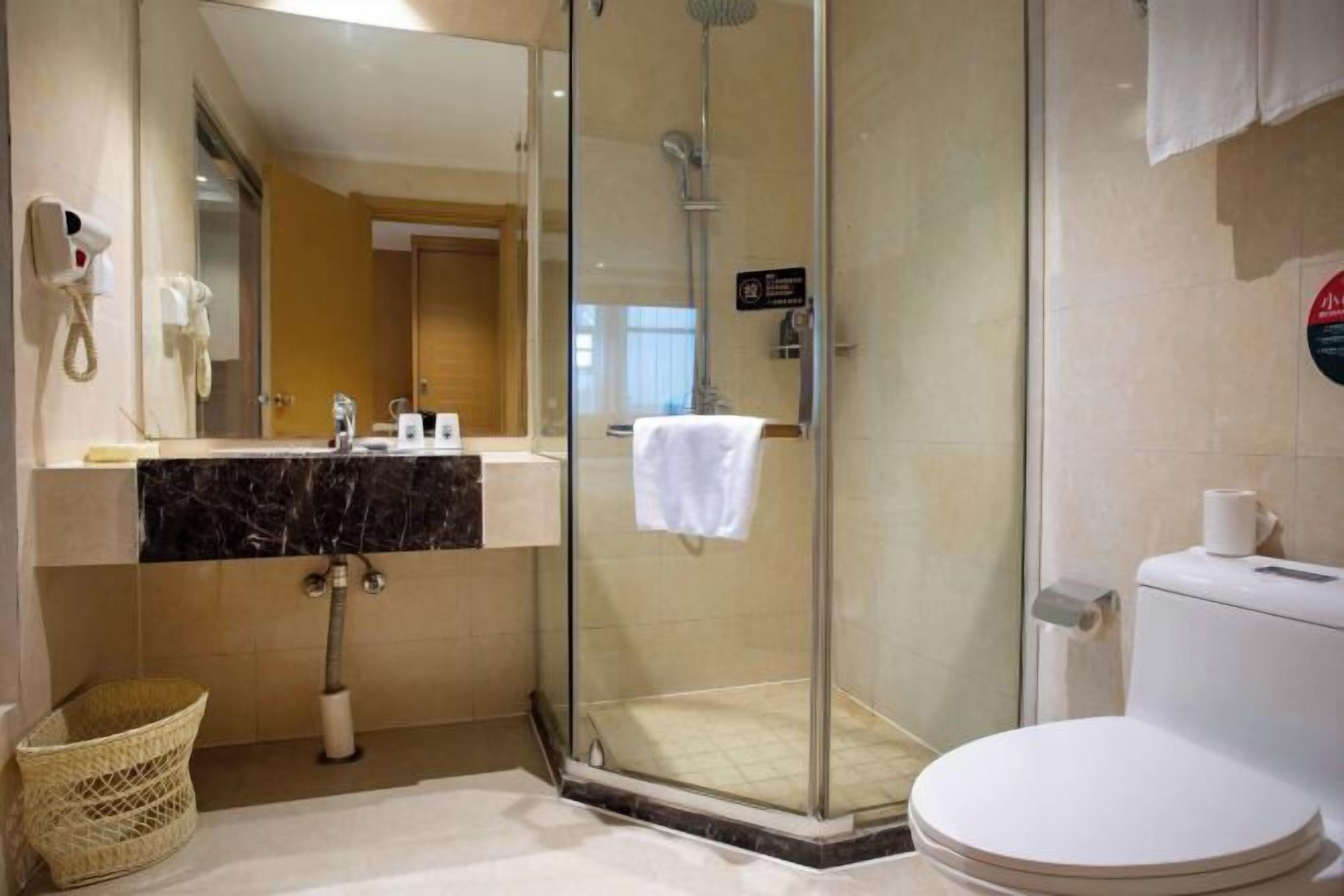 Een moderne badkamer met een douche in glazen cabine, een wit toilet, een marmeren wastafel en een grote spiegel.